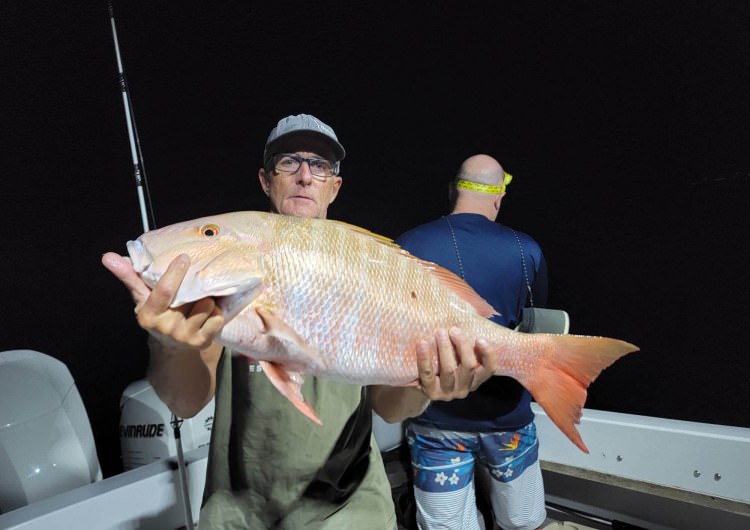 man holding a big fish on a boat at night